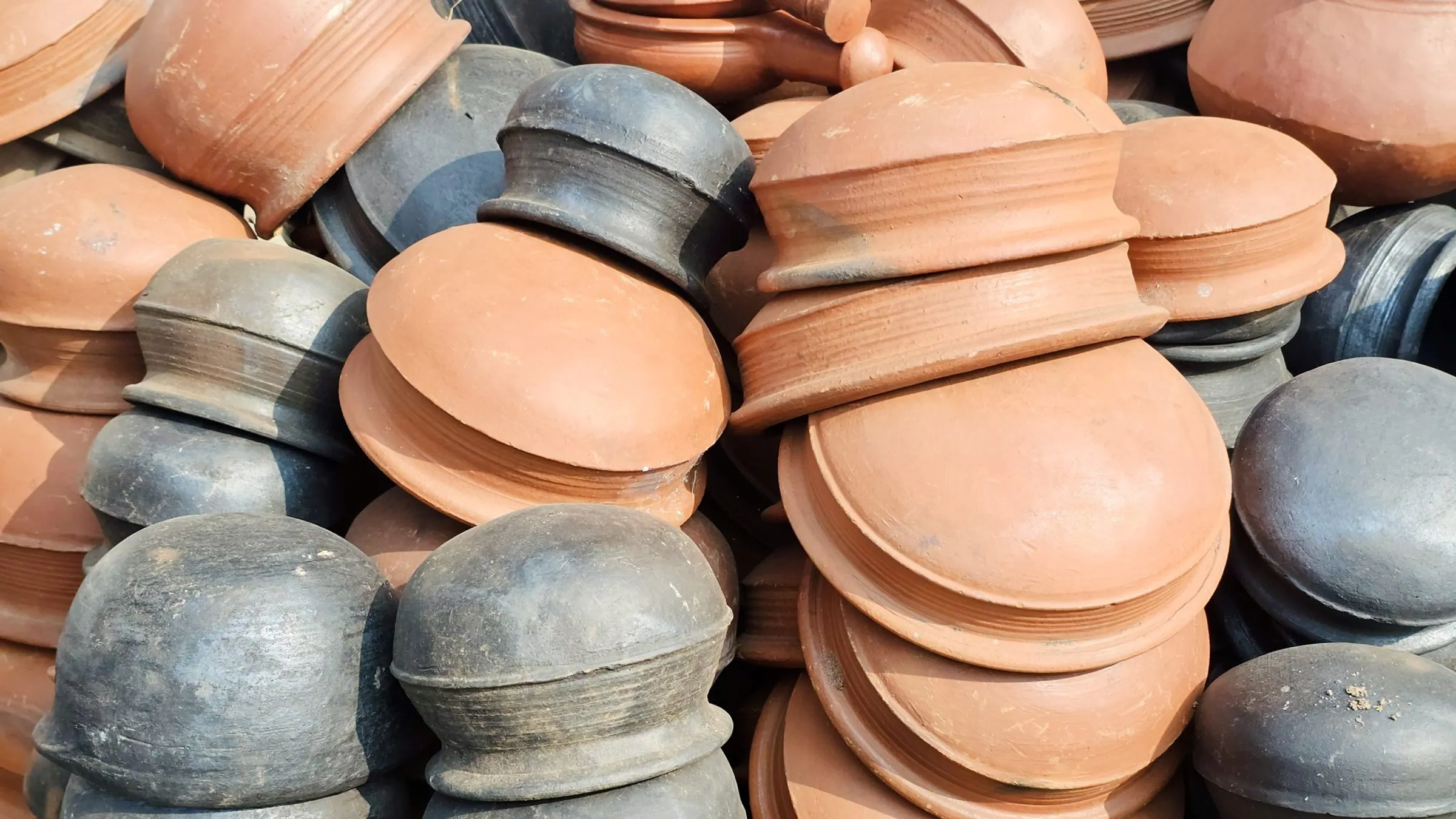 Piles of fired clay bowls and lids in terracotta and dark grey