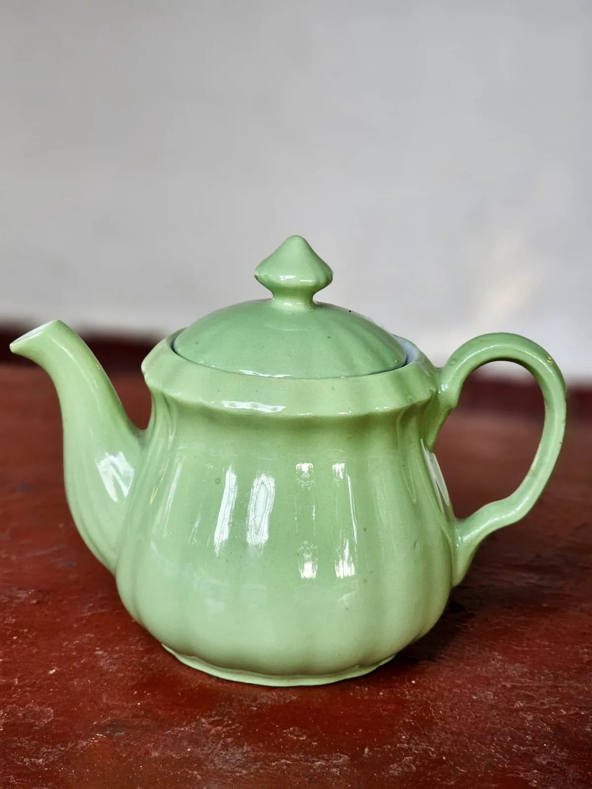 Pale green ceramic teapot on a dark red table